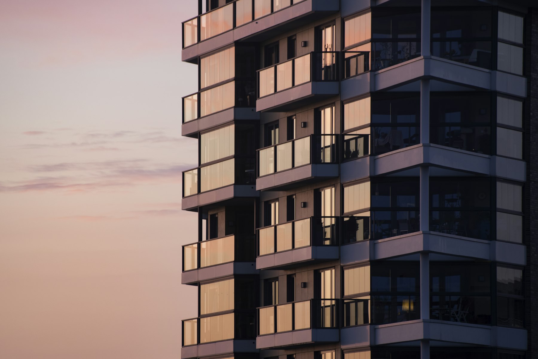 Fachada de un edificio residencial moderno con balcones vidriados al atardecer